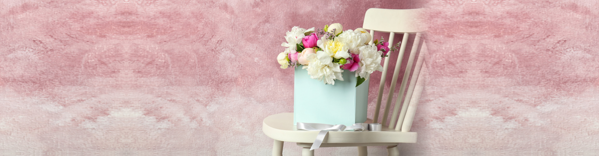 Box with beautiful flowers on wooden chair against color background